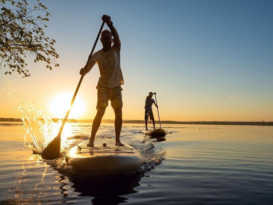 Two men paddle boarding against a sunset on a glassy lake